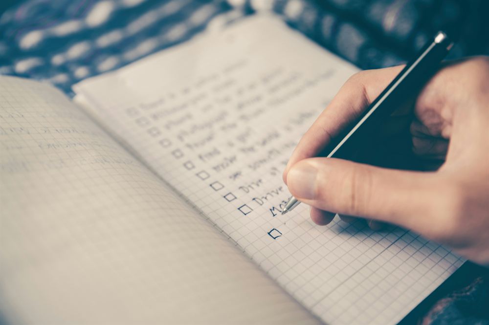A hand writing a handwritten checklist in a notebook.