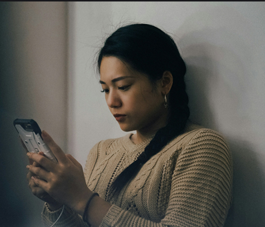A woman looking at her phone, representing reputational abuse.