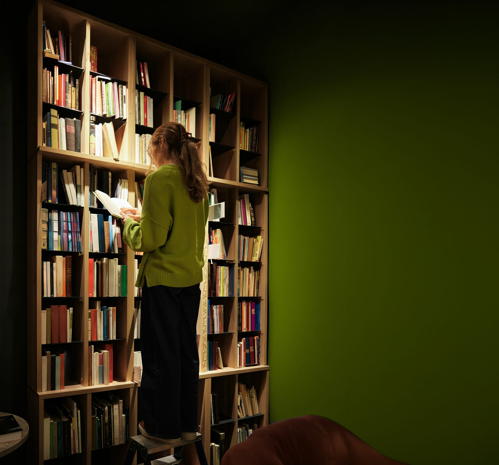 A woman in a yellow jumper browsing a shelf of books.
